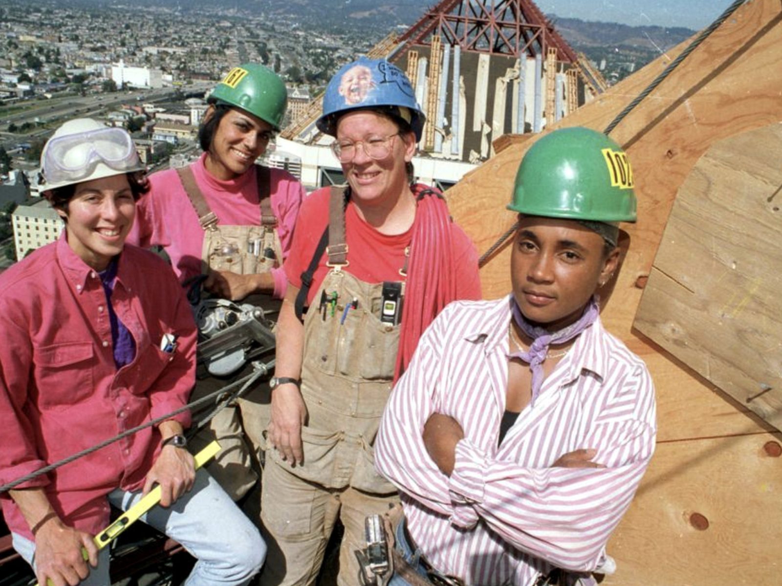 four tradeswomen in hard hats on a rooftop job site