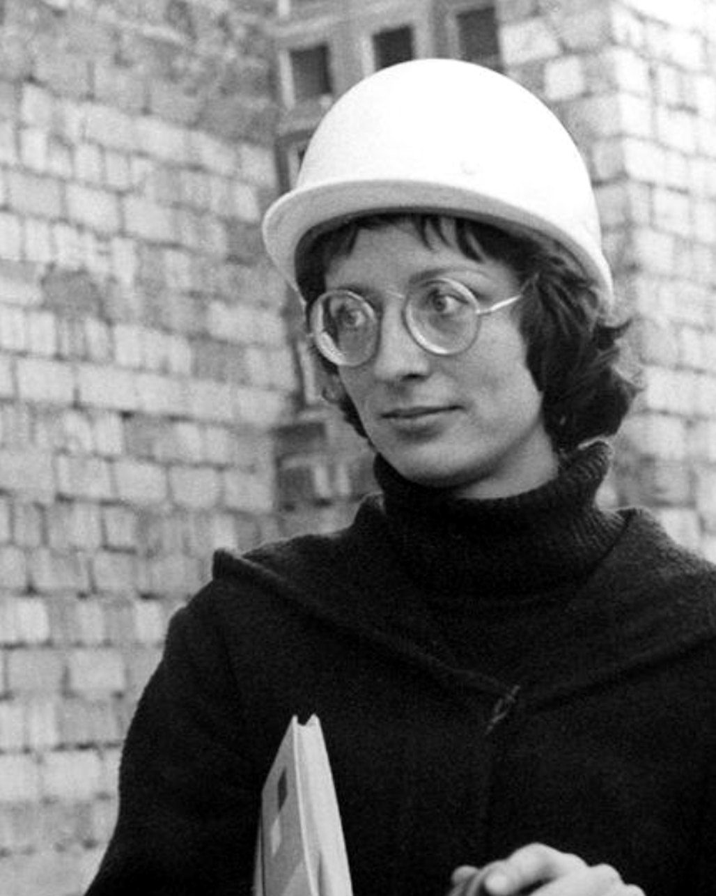 a woman in a hard hat and round glasses, black and white